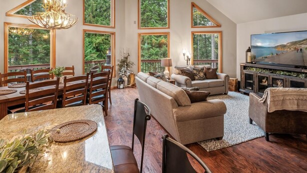 A spacious living room with a large sofa, a dining area with wooden chairs, and a television on a wooden cabinet. - Charming Secluded  3-bedroom house in Sagle ID close to Lake and Schweitzer Ski (Sagle)