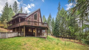 A two-story wooden cabin with a balcony, surrounded by a forested area. - Charming Secluded  3-bedroom house in Sagle ID close to Lake and Schweitzer Ski (Sagle)