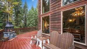 A wooden deck with Adirondack chairs, a stone fireplace, and a large window overlooking a forest. - Charming Secluded  3-bedroom house in Sagle ID close to Lake and Schweitzer Ski (Sagle)