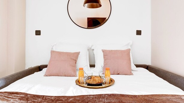 A neatly made bed with two pillows, a tray with croissants, juice, and glasses, and a round mirror on the wall. - TheBlueStay 39 – Cosy Apartment Buttes-Chaumont (Paris)