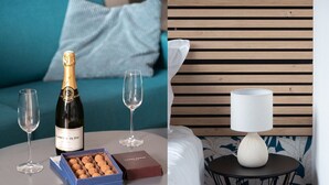A room with a round table, a bottle of champagne, two glasses, a box of chocolates, and a candle on a small round table.