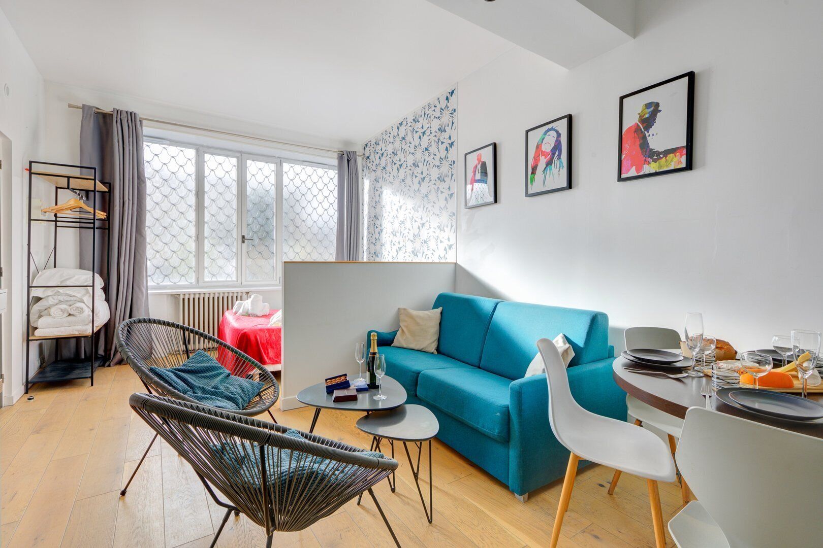 Una sala moderna con un sofá azul, una silla de mimbre, una mesita redonda y un comedor con una mesa y sillas blancas.