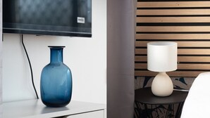 A modern room with a blue vase on a white dresser, a white lamp on a small round table, and a TV mounted on the wall.