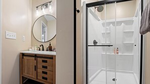 Un baño con tocador de madera, espejo redondo y cabina de ducha con paredes de vidrio.