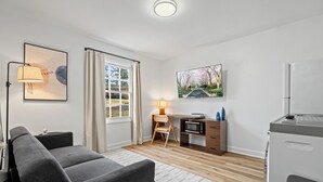 Una sala de estar moderna con un sofá gris, un escritorio con lámpara, un televisor y un refrigerador.