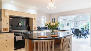 A modern kitchen with a central island, a dining area with chairs, and a view of the outdoors. - Superb 4BD Stay in Wyton and Houghton Village (Huntingdon)