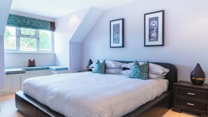 A bedroom with a large bed, a window with a view, and two framed pictures on the wall. - Superb 4BD Stay in Wyton and Houghton Village (Huntingdon)