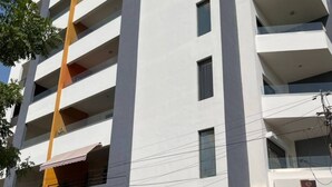 A multi-story building with a white facade and a yellow accent on the left side. There are balconies on each floor, and a car is parked in front of the building. - Cosy F3 in the center of Dakar (Dakar)