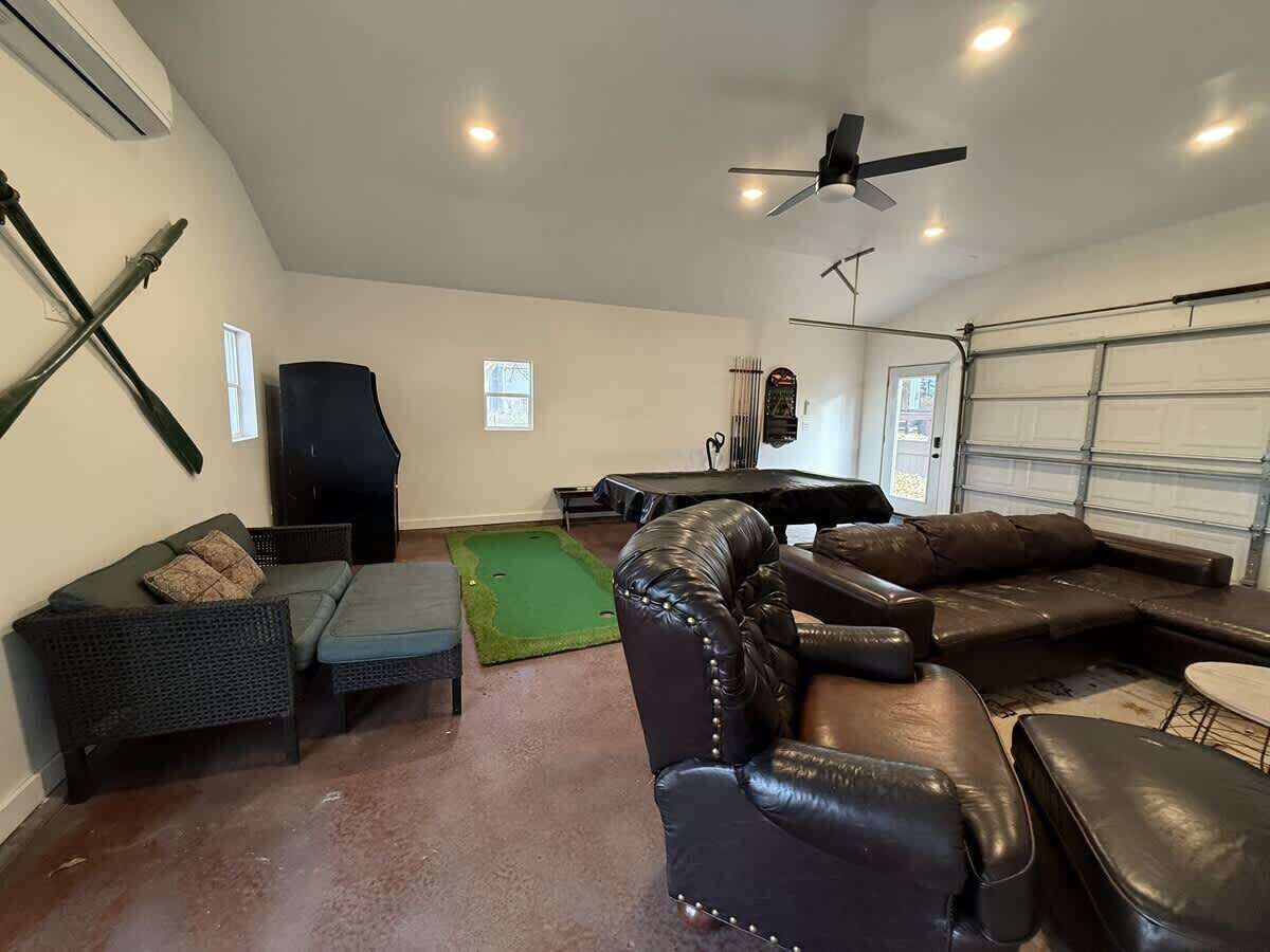 Ein geräumiges Wohnzimmer mit grünem Teppich, Ledersofas, einem Rattan-Sofa und einem Deckenventilator.