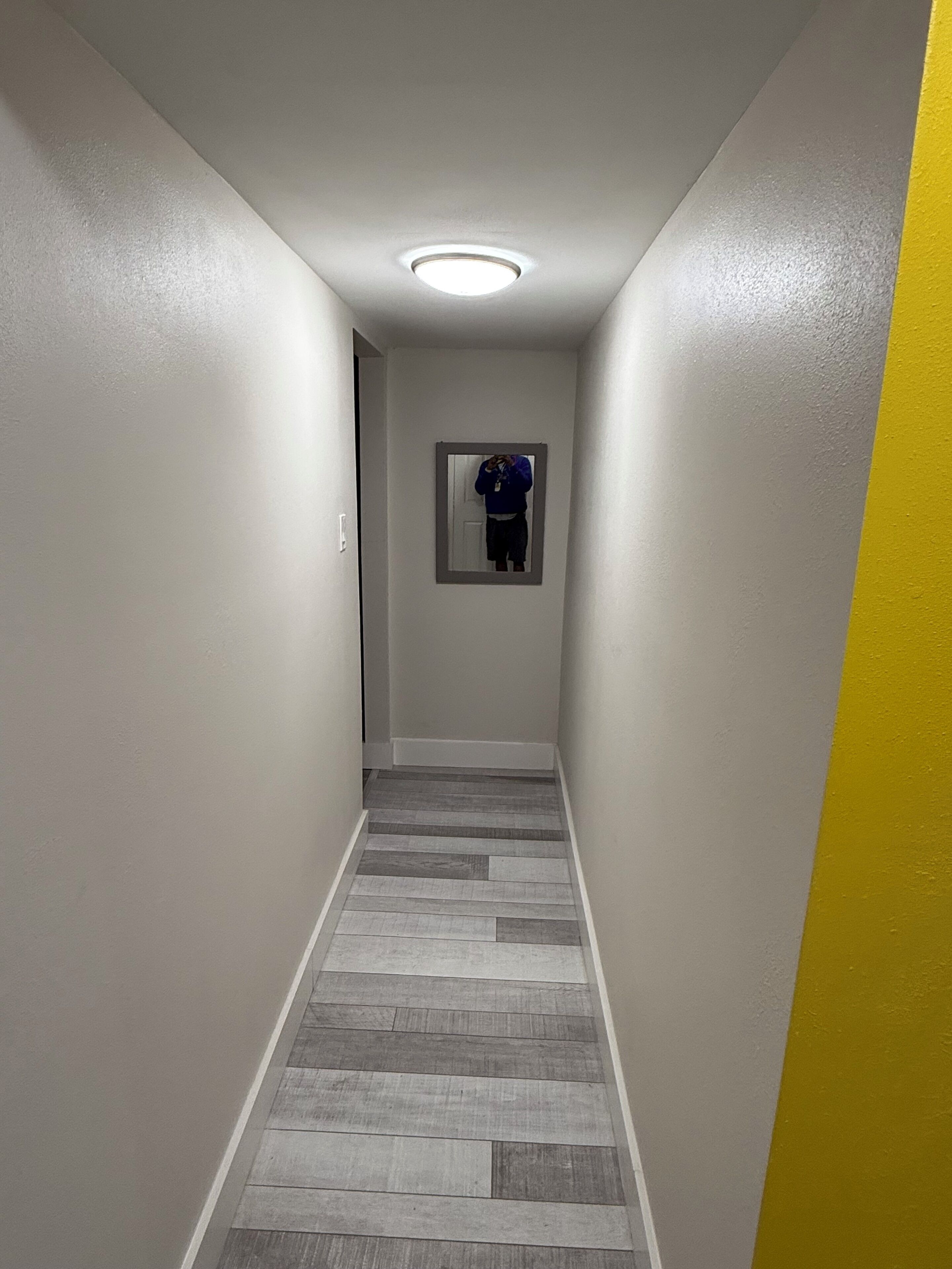 A narrow hallway with a wooden floor and a mirror on the wall.