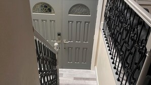 Una escalera con piso de mármol que lleva a una puerta gris con paneles de vidrio decorativos.