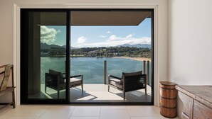 Une pièce dotée d’une grande porte-fenêtre coulissante donnant sur un balcon avec vue sur un lac et des montagnes. Il y a deux chaises sur le balcon.