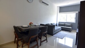 Un salon moderne comprenant un coin repas, un canapé gris, une table à manger avec des chaises, une horloge et un appareil de climatisation.