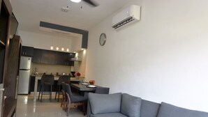 Une cuisine moderne avec des meubles de couleur sombre, un coin repas avec une table et des chaises, et un canapé gris dans l’espace salon.
