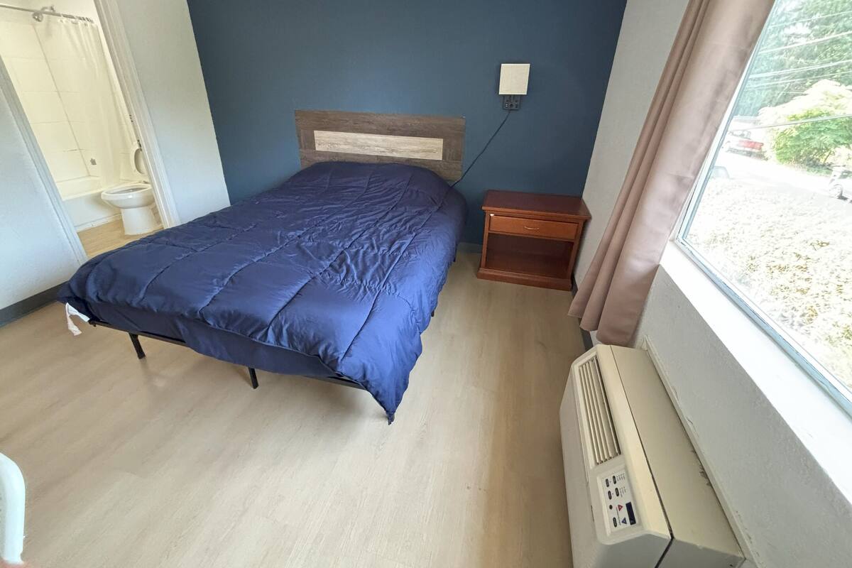 A bedroom with a bed, a nightstand, a window, and a radiator.