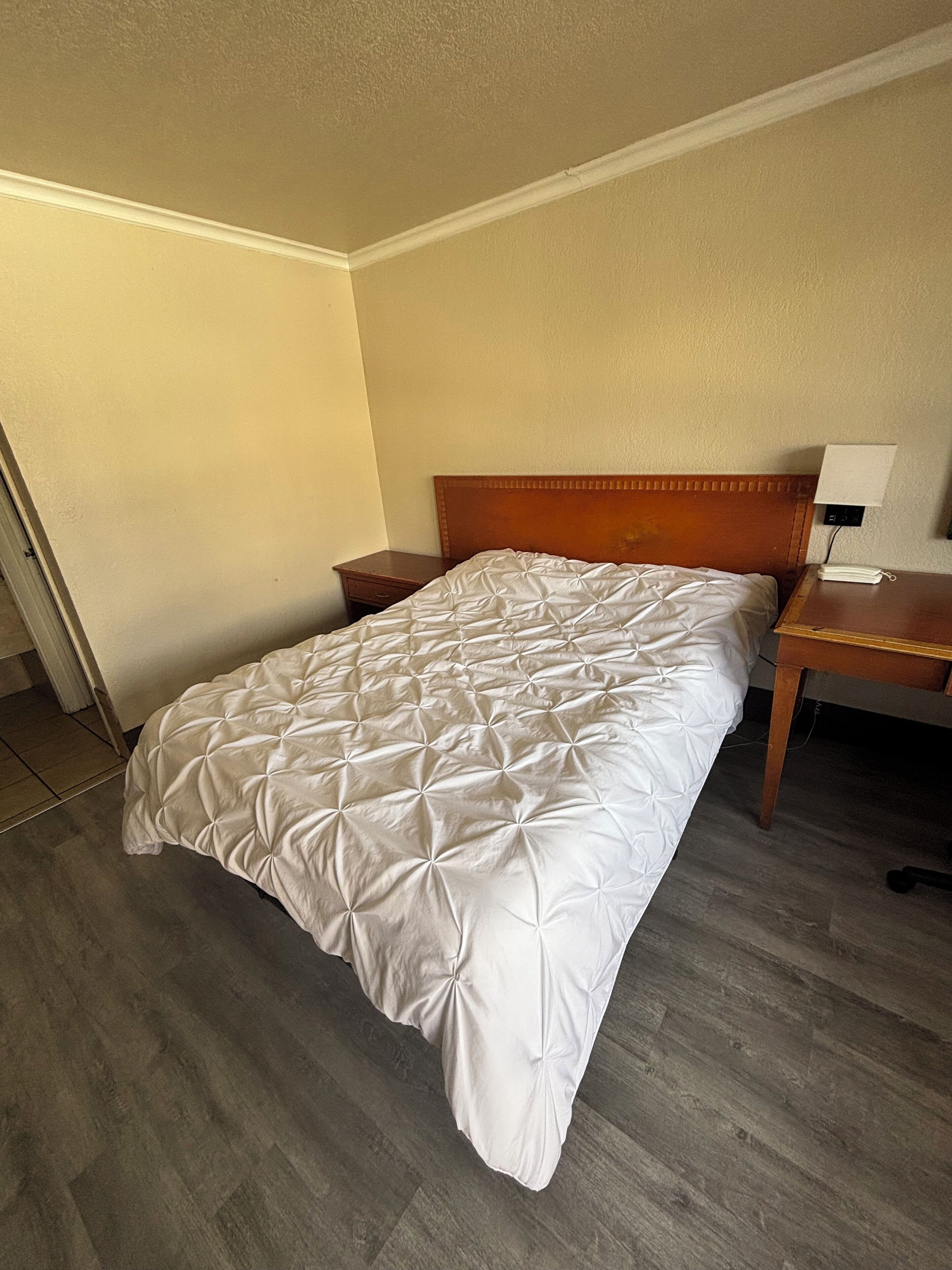 A single bed with a wooden headboard, a bedside table, and a nightstand with a lamp.