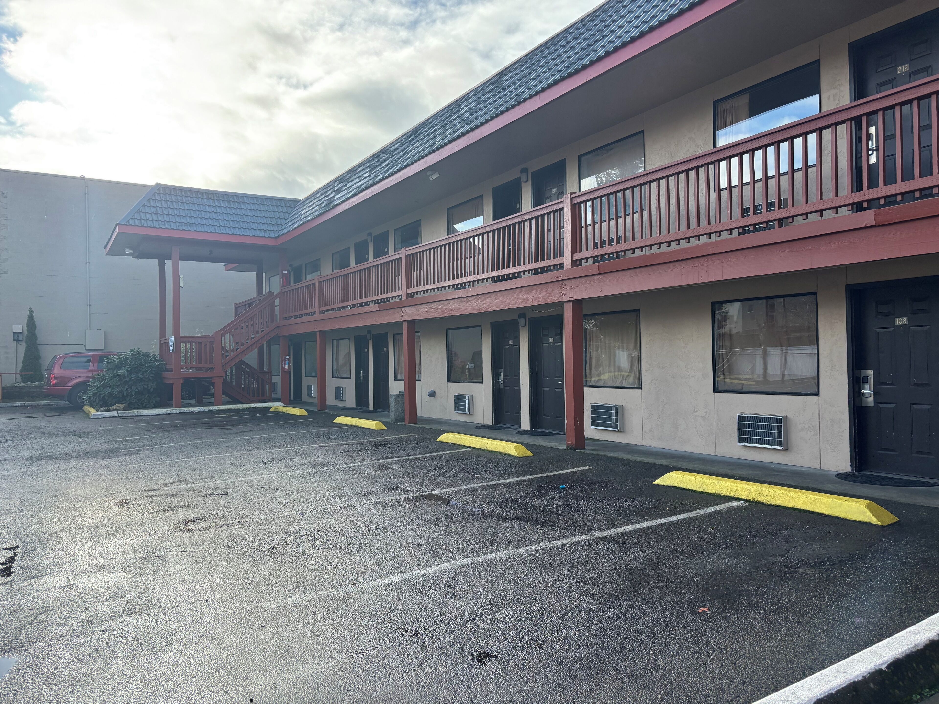 A motel with a red exterior, multiple balconies, and a parking lot with yellow curbs.