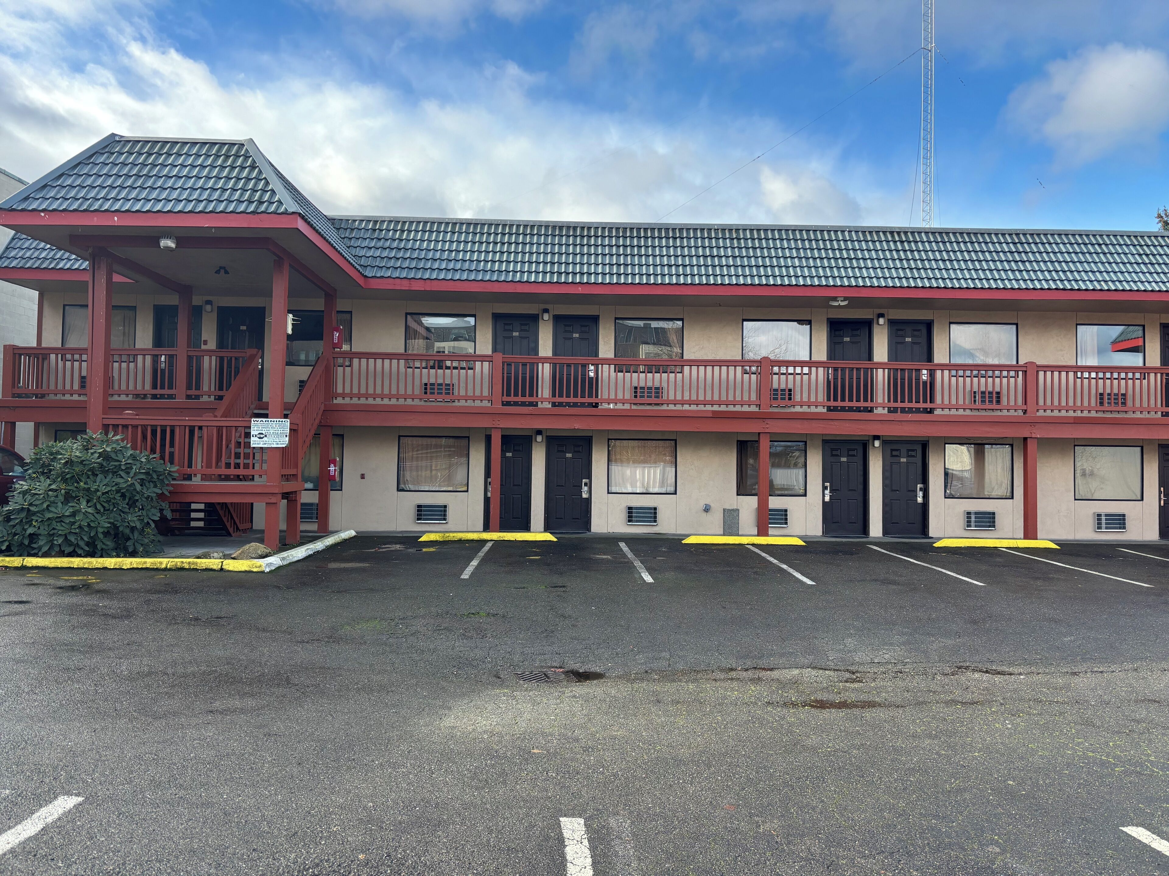 A two-story motel with a red exterior, multiple balconies, and a parking lot.