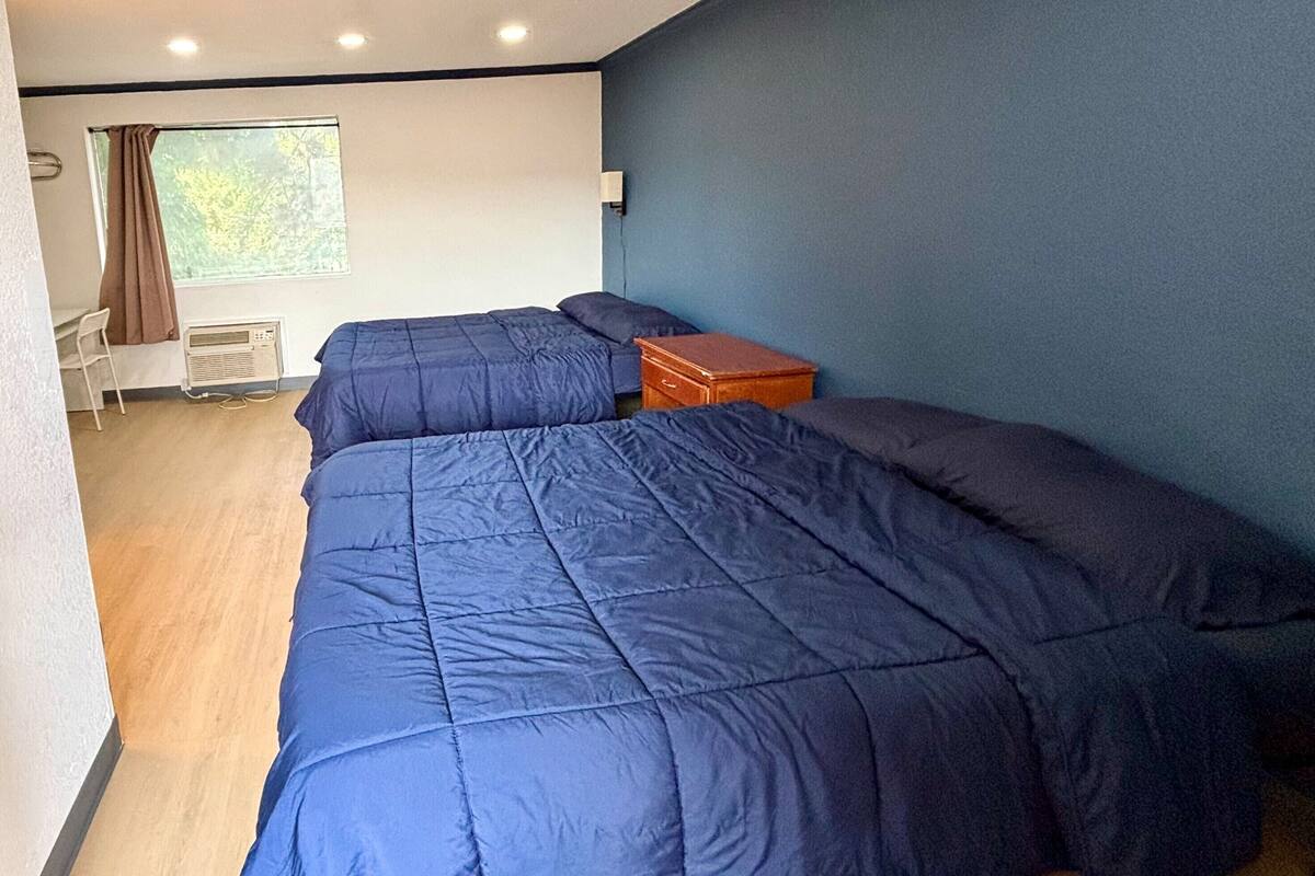 A bedroom with a large bed, a wooden nightstand, and a window with curtains.