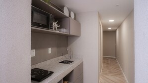 Una cocina compacta con microondas, estufa y lavamanos, y un pasillo con piso de madera.