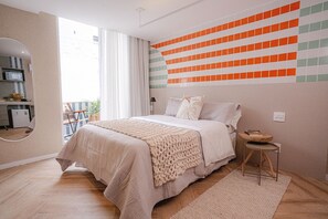 Relax in this serene bedroom with a large bed, a small table, and a chair, surrounded by a large mirror and a colorful geometric-patterned wall.