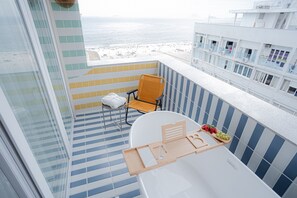 En balkon med en hvid stol, et lille bord med bakke, og udsigt til stranden.