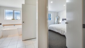 Una habitación de hotel moderna con un ventanal grande, una bañera, una cama con colcha blanca y una alfombra gris.