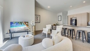 Una sala de estar moderna con un televisor de pantalla plana, sofás blancos y una zona de cocina con taburetes de bar.