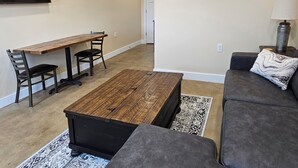 A living room with a sofa, a coffee table, a TV mounted on the wall, a dining table with chairs, and a framed picture. - Breckenridge Suites (Grove City)