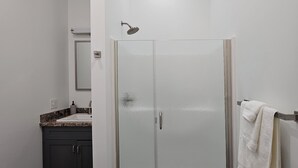 A narrow bathroom with a glass shower enclosure, a dark wood floor, and a white towel hanging on a rack. - Breckenridge Suites (Grove City)