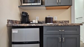 A compact kitchen with a built-in microwave, a coffee maker, a refrigerator, and dark cabinets. - Breckenridge Suites (Grove City)