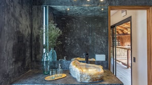A modern bathroom with a large mirror, a unique stone sink, and a glass shower enclosure. - Meteora Stay & Co-Working Space (Tulum)