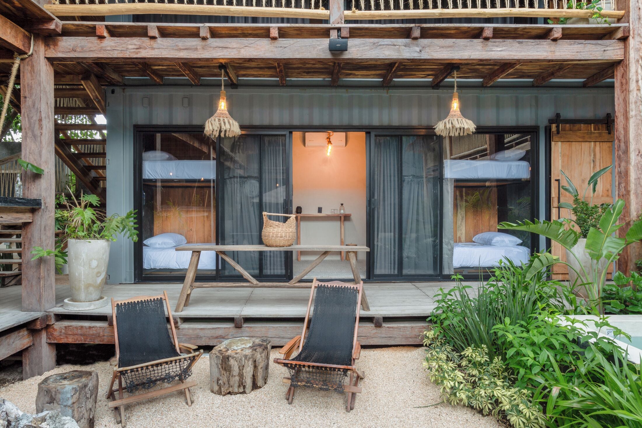 A rustic cabin with two bunk beds, a wooden deck, and a seating area with chairs and a table.
