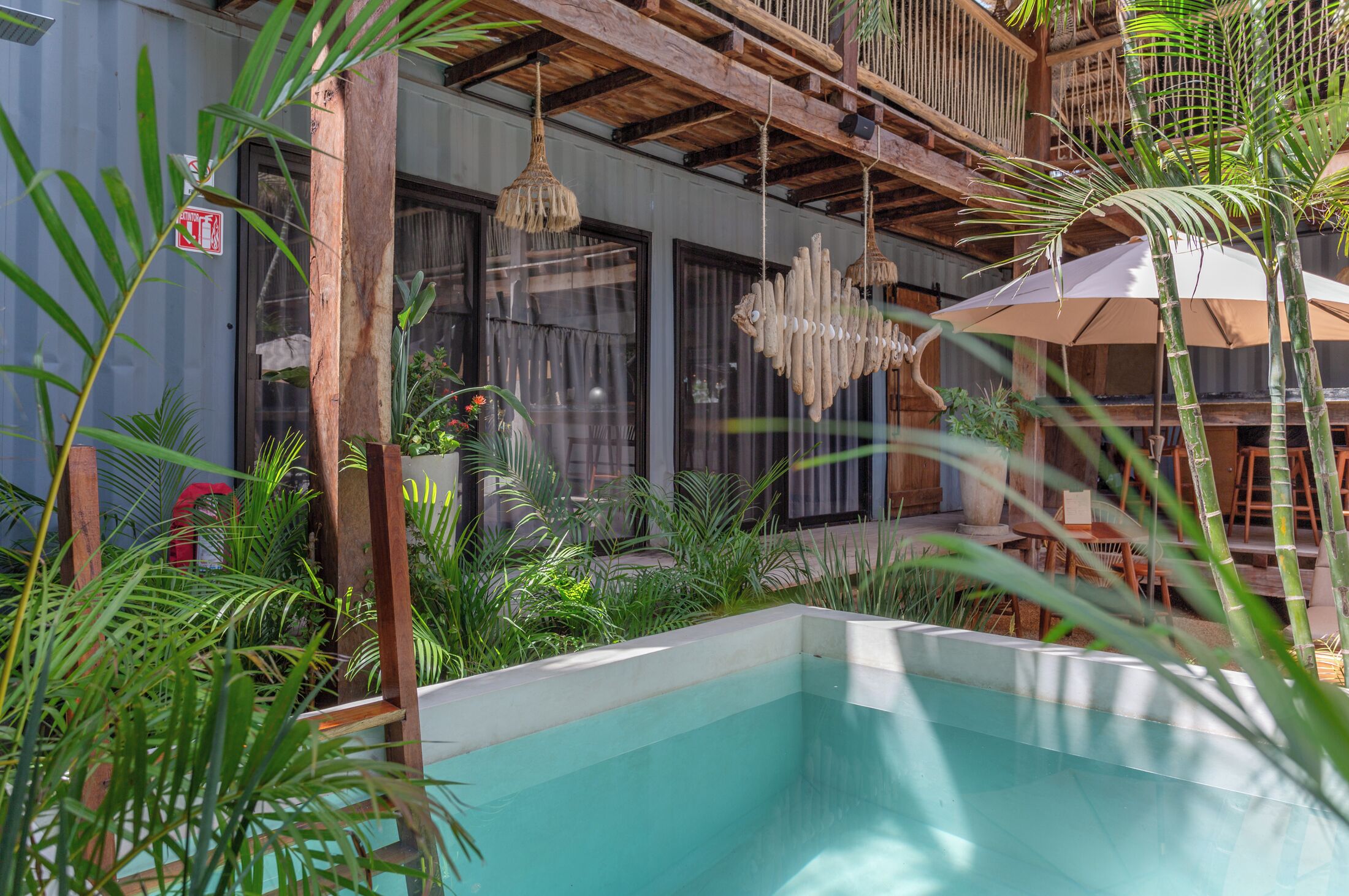 A pool area with a wooden deck, hanging lamps, and lush greenery.