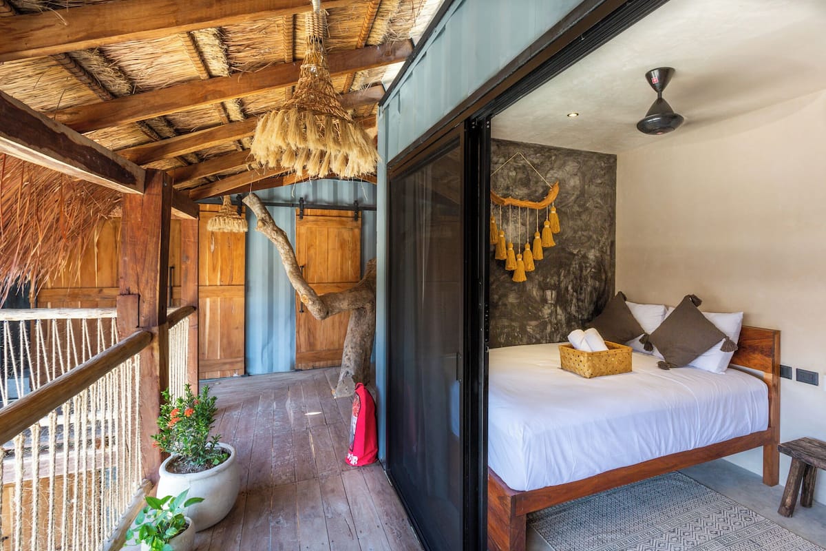 Une chambre avec un lit en bois, une grande fenêtre et un ventilateur de plafond.