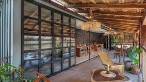 A spacious indoor area with large windows, wooden furniture, and a thatched ceiling. - Meteora Stay & Co-Working Space (Tulum)
