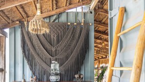 A rustic interior with a wooden table, two hexagonal stools, a hanging light fixture, and a woven wall hanging. - Meteora Stay & Co-Working Space (Tulum)