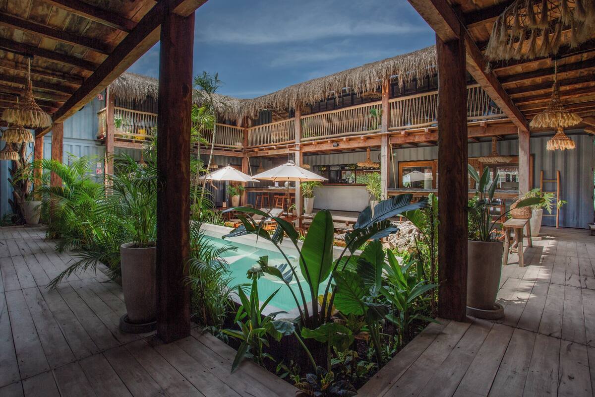 Une terrasse en bois avec une piscine, entourée de plantes en pot et de parasols.