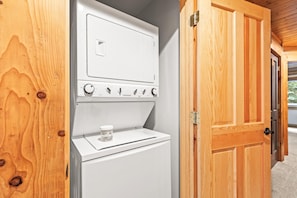 A compact laundry area with a washer and dryer, wooden doors, and a small container of laundry soap. - Walk to Ski Slopes + Trails! Cozy 2-Bedroom, Recently Renovated Condo with Pool, Hot Tub, BBQ, and A/C | BBL-351A by KBM Resorts (Park City)