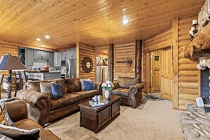 Interior de una cabaña de madera con sala de estar que incluye sofás de cuero, una mesa de centro y una chimenea.