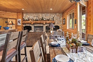 A rustic cabin interior with a stone fireplace, wooden dining area, and a cozy seating arrangement. - Walk to Ski Slopes + Trails! Cozy 2-Bedroom, Recently Renovated Condo with Pool, Hot Tub, BBQ, and A/C | BBL-351A by KBM Resorts (Park City)