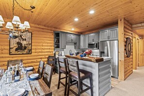 Interior de una cabaña de madera con cocina que incluye gabinetes grises, un refrigerador de acero inoxidable y un comedor con mesa y sillas de madera.