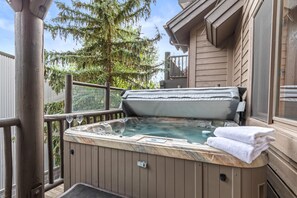 Un jacuzzi en una terraza de madera con vistas a árboles y un edificio.