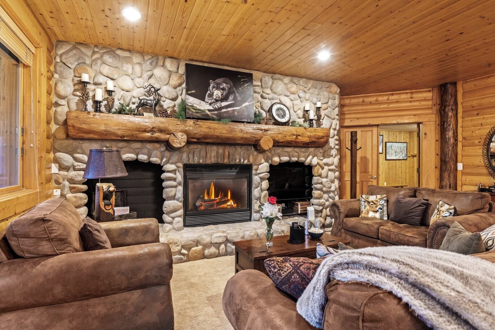 Un acogedor interior de cabaña con chimenea de piedra, muebles de cuero y decoración de pared con temática de oso.