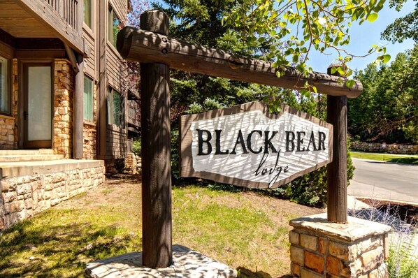 Un panneau en bois sur lequel est inscrit « BLACK BEAR lodge », soutenu par deux poteaux en bois et reposant sur une base en pierre.