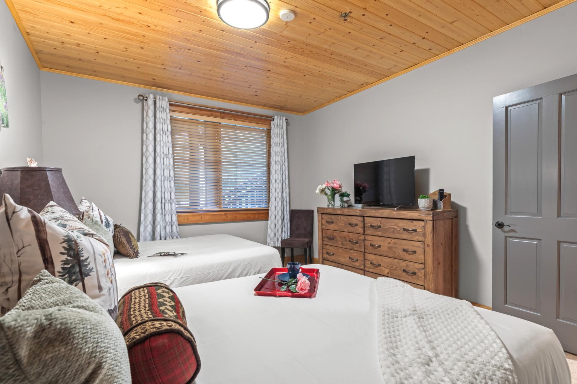 Un dormitorio con techo de madera, una cama, un aparador, un televisor y una ventana con persianas.