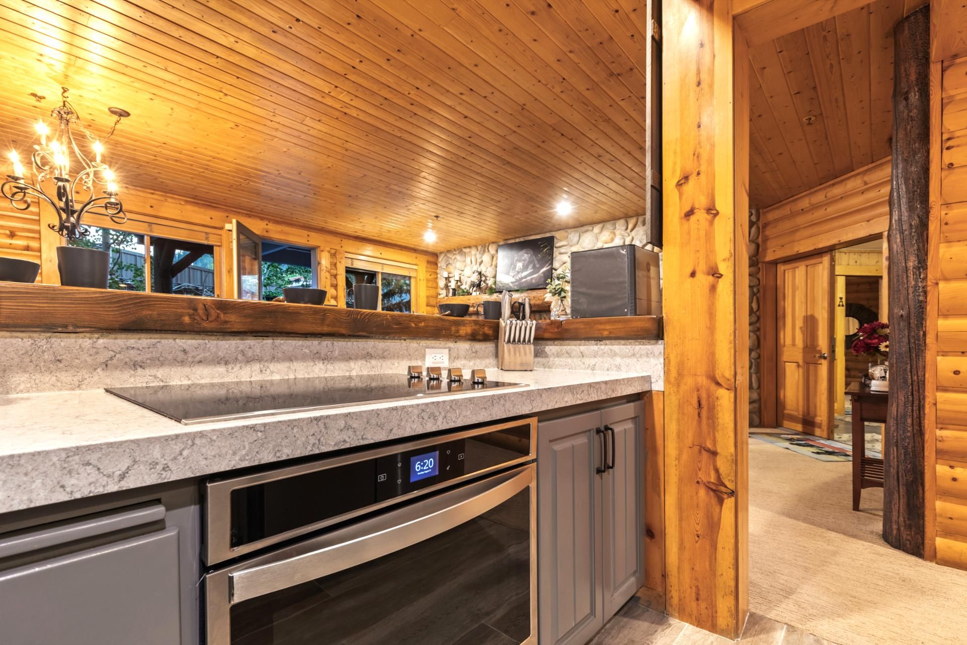 A modern kitchen with a marble countertop, stainless steel appliances, and wooden ceiling.
