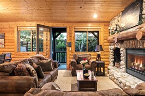 A log cabin interior with a fireplace, leather sofas, and a stone fireplace surround.
