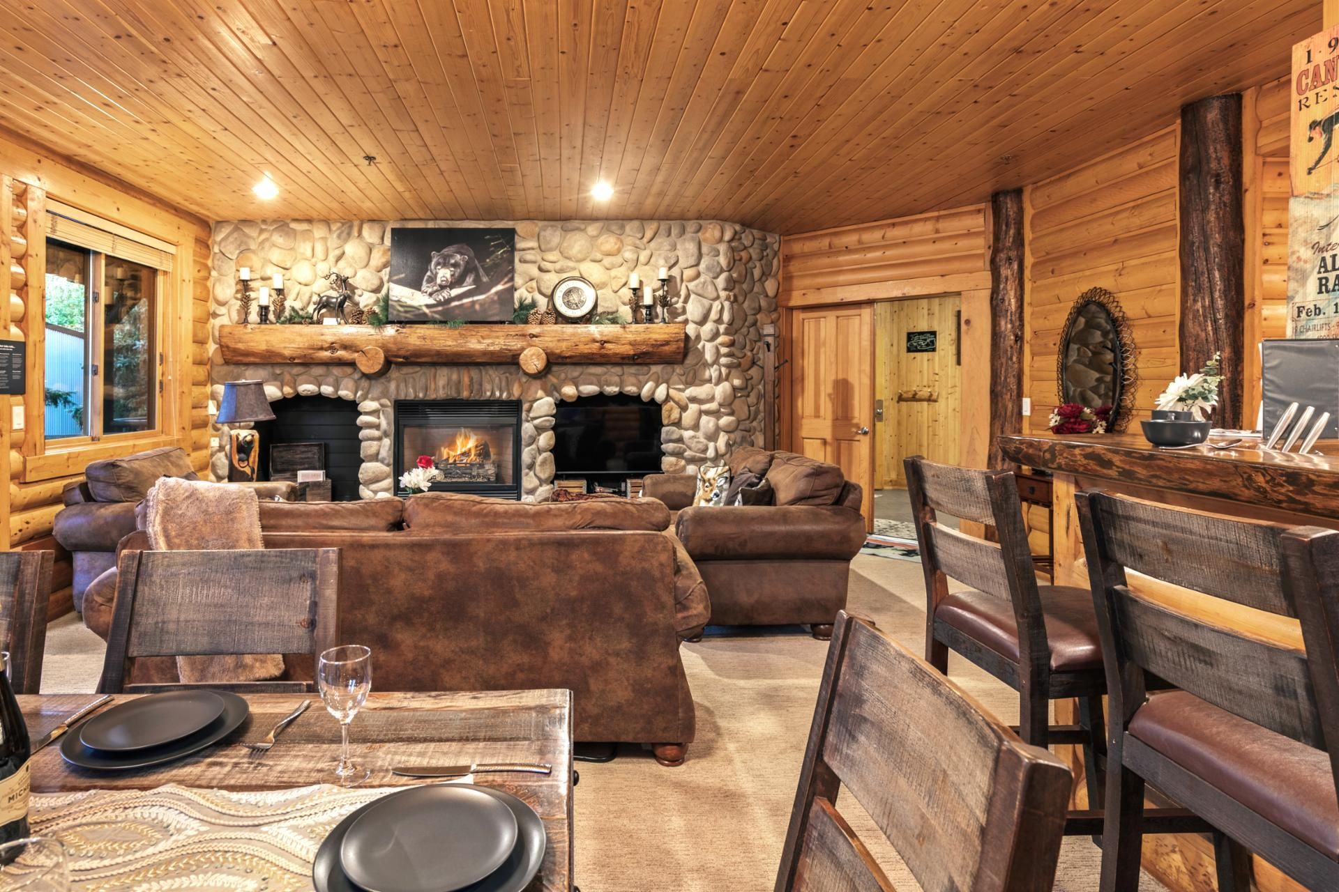 A log cabin interior with a stone fireplace, wooden furniture, and a dining area.