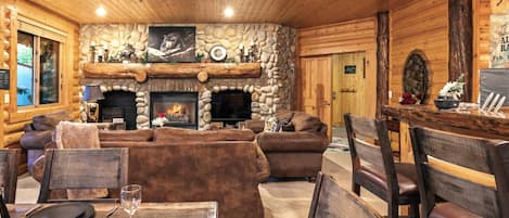 A log cabin interior with a stone fireplace, wooden furniture, and a dining area.